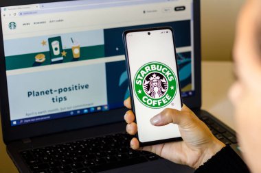 18 Nisan 2022, Brezilya. Bu resimde, bir kadın Starbucks logosunun ekranda sergilendiği ve arka planda Starbucks 'ın web sitesinin sergilendiği bir akıllı telefon tutuyor.