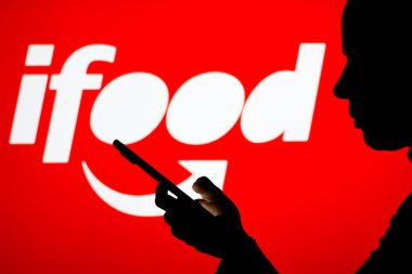 18 Nisan 2022, Brezilya. Bu resimde iFood logosu, elinde cep telefonu olan siluet bir kadının arka planında görülüyor.
