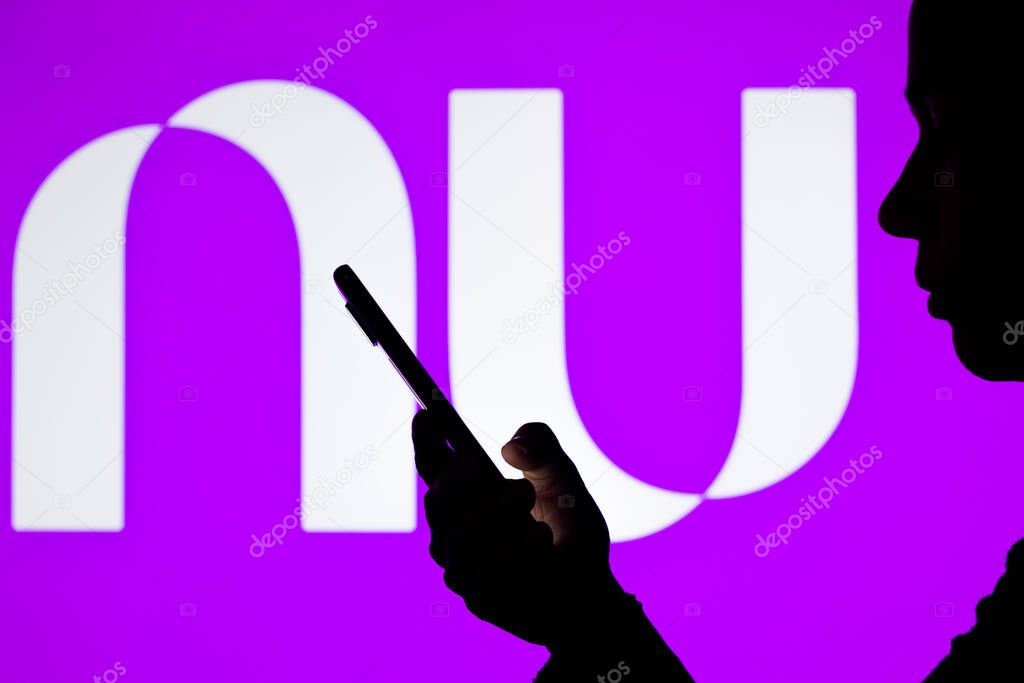 April 18, 2022, Brazil. In this photo illustration the Nubank logo seen in the background of a silhouette woman holding a mobile phone