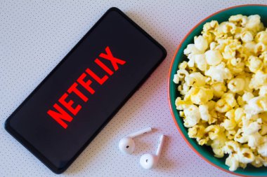 19 Nisan 2022, Brezilya. Bu resimde Netflix logosu bir kase patlamış mısır ve kulaklıkla birlikte akıllı bir telefonda sergileniyor.