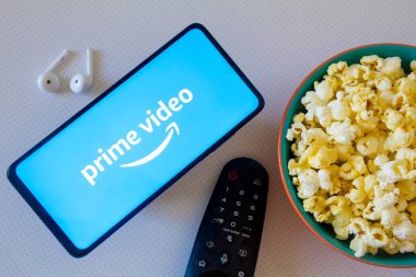 19 Nisan 2022, Brezilya. Bu resimde, Amazon Prime video logosu akıllı bir telefonda bir kase patlamış mısır, kulaklık ve uzaktan kumandayla birlikte görülüyor.