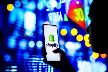22 Nisan 2022, Brezilya. Bu resimde, siluetli bir kadın ekranda Shopify logosu olan bir akıllı telefon tutuyor.