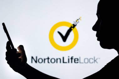 27 Nisan 2022, Brezilya. Bu resimde, NortonLifeLock logosu siluetli bir kadının elinde cep telefonu ile arka planda görülüyor.