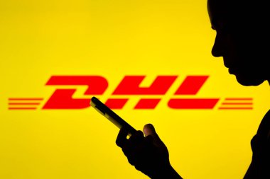 29 Nisan 2022, Brezilya. Bu resimde DHL logosu, elinde cep telefonu olan siluetli bir kadının arka planında görülüyor.