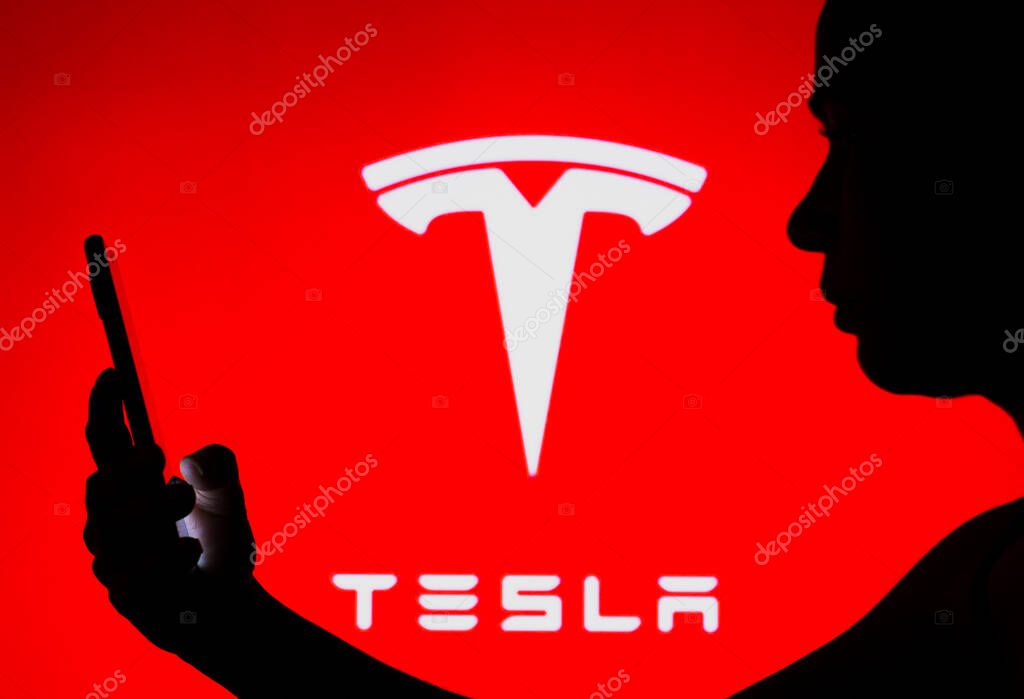 May 2, 2022, Brazil. In this photo illustration, the Tesla, Inc. logo is seen in the background of a silhouetted woman holding a mobile phone