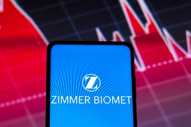 May 4, 2022, Brazil. In this photo illustration the Zimmer Biomet logo seen displayed on a smartphone screen, with graphic representation of the stock market in the background