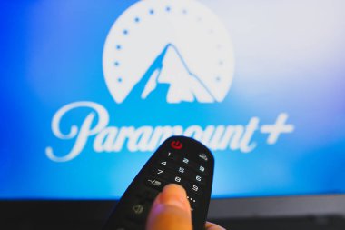 May 10, 2022, Brazil. In this photo illustration a close-up of a hand holding a TV remote control seen in front of the Paramount Plus logo