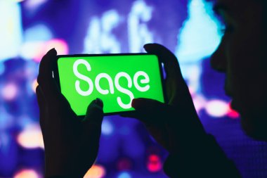 11 Haziran 2022, Brezilya. Bu resimde, siluetli bir kadın ekranda Sage Group logosu olan bir akıllı telefon tutuyor.