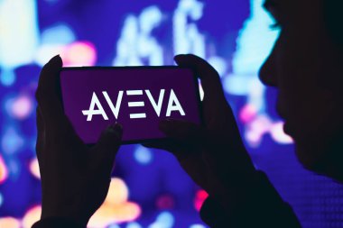 11 Haziran 2022, Brezilya. Bu resimde, siluetli bir kadın ekranda AVEVA Grubu logosu olan bir akıllı telefon tutuyor.