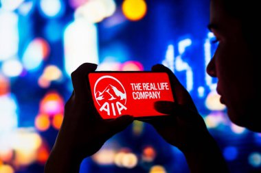 June 28, 2022, Brazil. In this photo illustration, a silhouetted woman holds a smartphone with the AIA Group Limited logo displayed on the screen