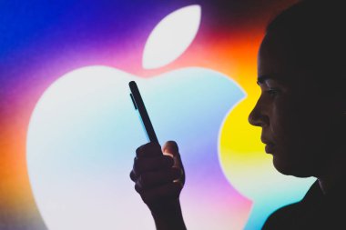June 29, 2022, Brazil. In this photo illustration, the Apple Inc. logo is seen in the background of a silhouetted woman holding a mobile phone
