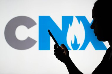 July 5, 2022, Brazil. In this photo illustration, the CNX Resources Corporation logo is seen in the background of a silhouetted woman holding a mobile phone