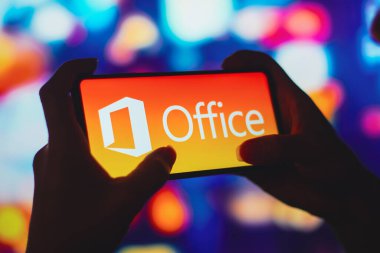 6 Temmuz 2022, Brezilya. Bu resimde siluetli bir kadın ekranda Microsoft Ofis logosu olan bir akıllı telefon tutuyor.