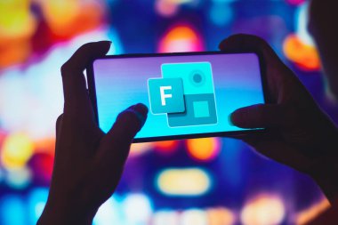 July 6, 2022, Brazil. In this photo illustration, a silhouetted woman holds a smartphone with the Microsoft Forms logo displayed on the screen