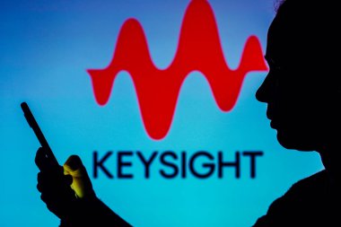August 12, 2022, Brazil. In this photo illustration, the Keysight Technologies logo is seen in the background of a silhouetted woman holding a mobile phone
