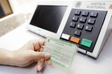 2 Ekim 2022, Brezilya. Bu fotoğraf illüstrasyonunda Brezilya seçimlerinde zorunlu unsur olan Seçmen Belgesi (Oy Verme Lisansı) bulunur. Arka planda elektronik bir vazo oy sandığı var.