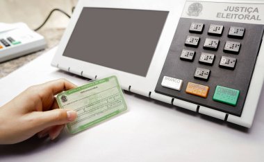 2 Ekim 2022, Brezilya. Bu fotoğraf illüstrasyonunda Brezilya seçimlerinde zorunlu unsur olan Seçmen Belgesi (Oy Verme Lisansı) bulunur. Arka planda elektronik bir vazo oy sandığı var.