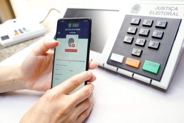 2 Ekim 2022, Brezilya. Bu resimde, akıllı telefon ekranınızdaki E-Başlık uygulaması var. Arka planda elektronik bir vazo oy sandığı var.