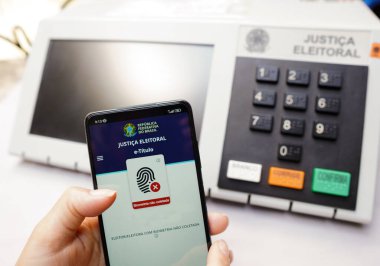 2 Ekim 2022, Brezilya. Bu resimde, akıllı telefon ekranınızdaki E-Başlık uygulaması var. Arka planda elektronik bir vazo oy sandığı var.