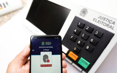 2 Ekim 2022, Brezilya. Bu resimde, akıllı telefon ekranınızdaki E-Başlık uygulaması var. Arka planda elektronik bir vazo oy sandığı var.