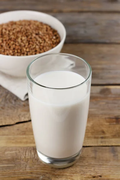 Mléko bez pohankového mléka ve sklenici a semena v misce na dřevěném pozadí — Stock fotografie