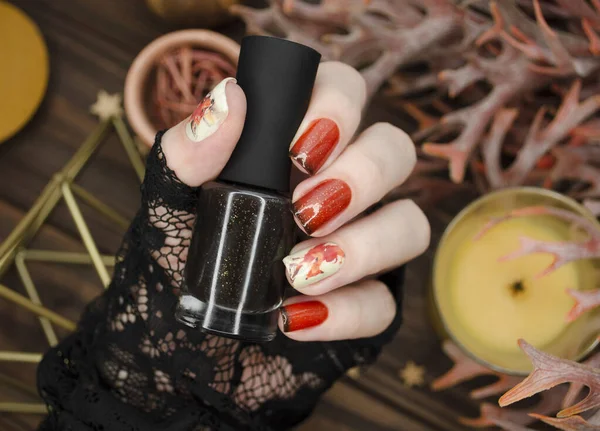 Orange glitter nails with black tips on a cozy hygge style background. Winter fall nail style