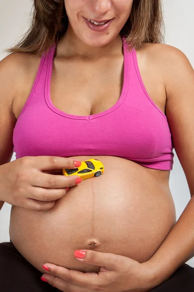 怀孕的女人，在她的肚子里玩着一辆玩具车 — 图库照片
