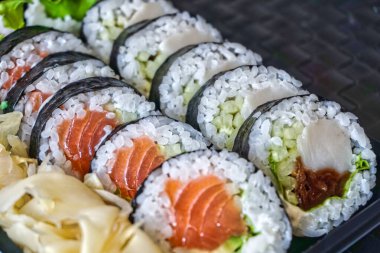 Dilimlenmiş somon ruloları ve plastik kabın içinde çiğ ton balığı suşisi.