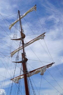 Tall ship mast with rolled sails, sky in background