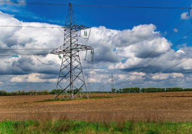 Kablolu yüksek voltajlı güç iletim kulesi. Yüksek voltaj hattı. Enerji endüstrisi. Enerji transferi. Mavi gökyüzü. Beyaz bulutlar. Tarım alanı. Bulutlu ufuk. İş için. Elektrikçi işi..
