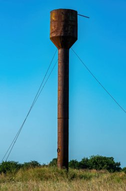 Mavi gökyüzüne karşı tarlada eski paslı su kulesi. Su kulesi. Endüstriyel ekipman Metal yapı. Mavi gökyüzü. Güneşli bir gün. Yükseğe. Kırsal kesimde. Arkaplan resmi.