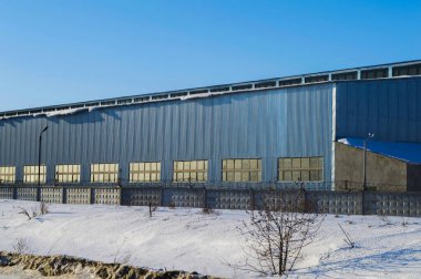 Pencereli paslanmaz çelikten yapılmış endüstriyel bir bina. Fabrikanın üretim atölyesi. Endüstriyel bina. Paslanmaz çelik. Cam pencereler. Kış mevsimi. Mavi gökyüzü. Sanayi.