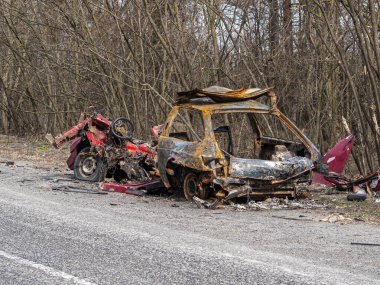 Road traffic accident of a car with fire. Car accident. Road in the forest. Damaged transport. Asphalt pavement. Traffic Laws. Military actions. Motor vehicle. Ukraine.