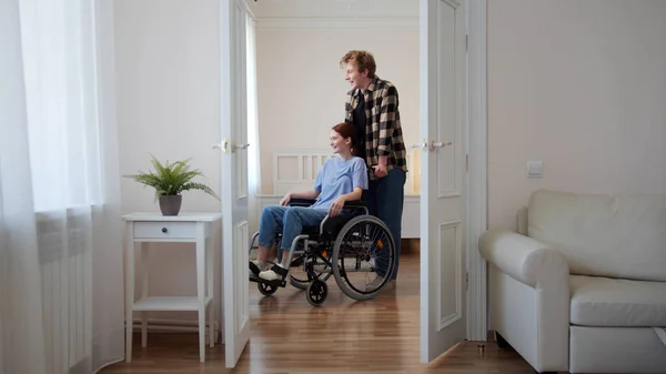 Bir adam kız arkadaşını tekerlekli sandalyeye oturtuyor. — Stok fotoğraf