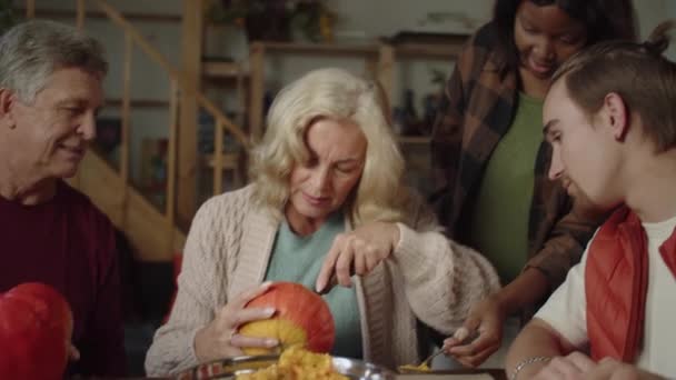 Une femme en pull beige sort la pulpe d'une citrouille, et le reste de la famille se tient à proximité et regarde comment elle va — Video