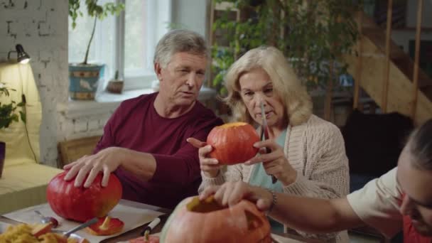 Elderly woman carves a lantern from a pumpkin and consults with her husband and adult son — Stock Video