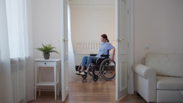 Een jonge gehandicapte vrouw rijdt in haar rolstoel door de kamer en strekt zich uit — Stockvideo