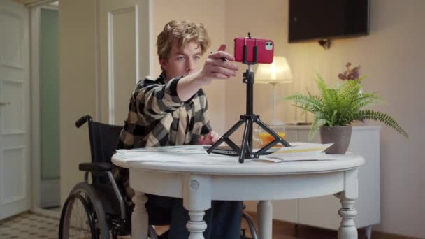 Mladý zdravotně postižený muž pozdravuje někoho na internetu a ukazuje grafy — Stock video