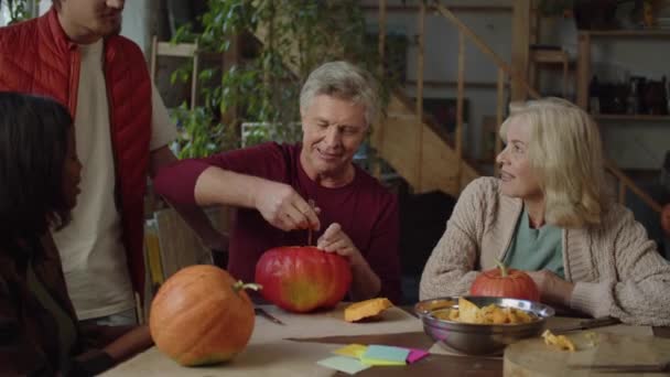 La famiglia si siede a tavola e guarda un uomo anziano sbucciare una zucca dalla polpa — Video Stock