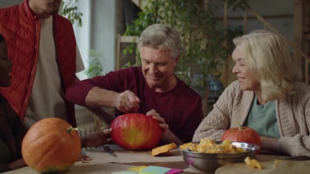 Sedmdesátiletý muž sedí u stolu se svou rodinou a čistí dýni ze semen — Stock video