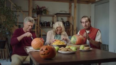 Yaşlı ebeveynleri olan genç bir adam masada oturuyor ve Cadılar Bayramı için lamba kesiyor.