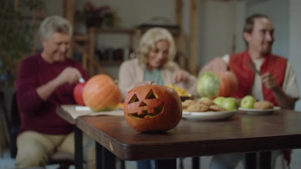 En græskar lampe står på bordet. I baggrunden forbereder en familie sig på Halloween. – Stock-video