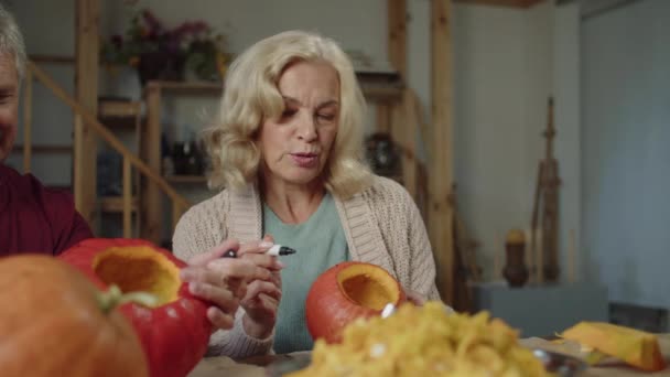 Couple âgé dessiner ensemble sur des citrouilles avec un marqueur et parler — Video