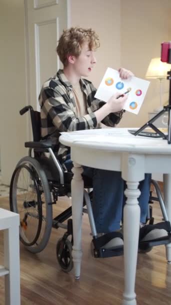 A disabled young man is talking with someone and showing diagrams — Stock Video