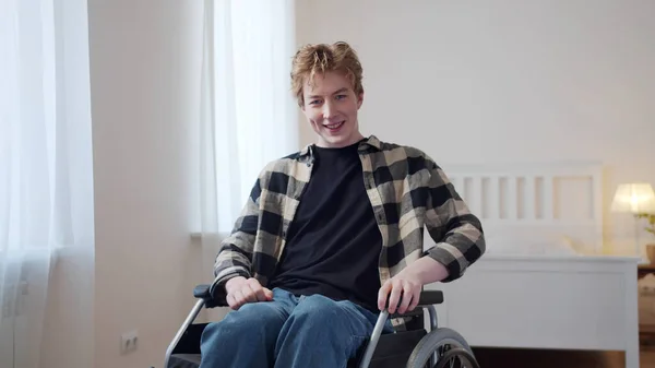 En ung handikappad man sitter i rullstol i rummet och tittar in i kameran — Stockfoto
