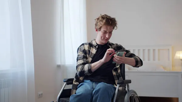 Un hombre discapacitado está sentado en su silla de ruedas y mirando a través de Internet — Foto de Stock