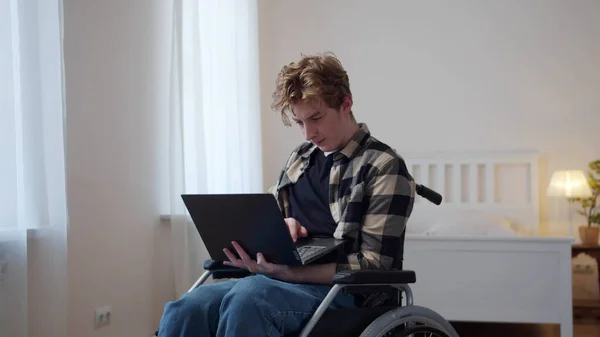 Un hombre discapacitado está sentado en su silla de ruedas y mirando a través de Internet — Foto de Stock