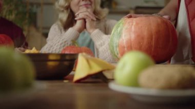 Bir adam yemek masasına ailesiyle birlikte balkabağı oyuyor.