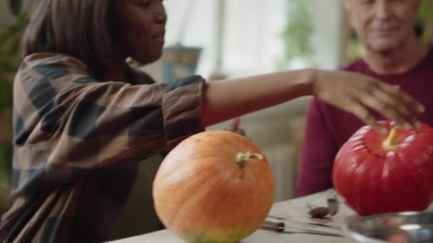 Vieja sentada a la mesa y enseñándole a una joven una calabaza para Halloween — Vídeo de stock