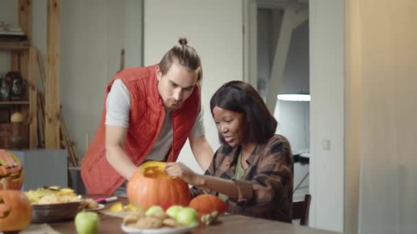 Los amigos tallan una lámpara de calabaza juntos. Se divierten hablando y discutiendo pasatiempos — Vídeo de stock